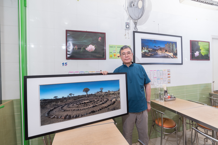 老闆陳烱康展示掛於店內自己的攝影作品。